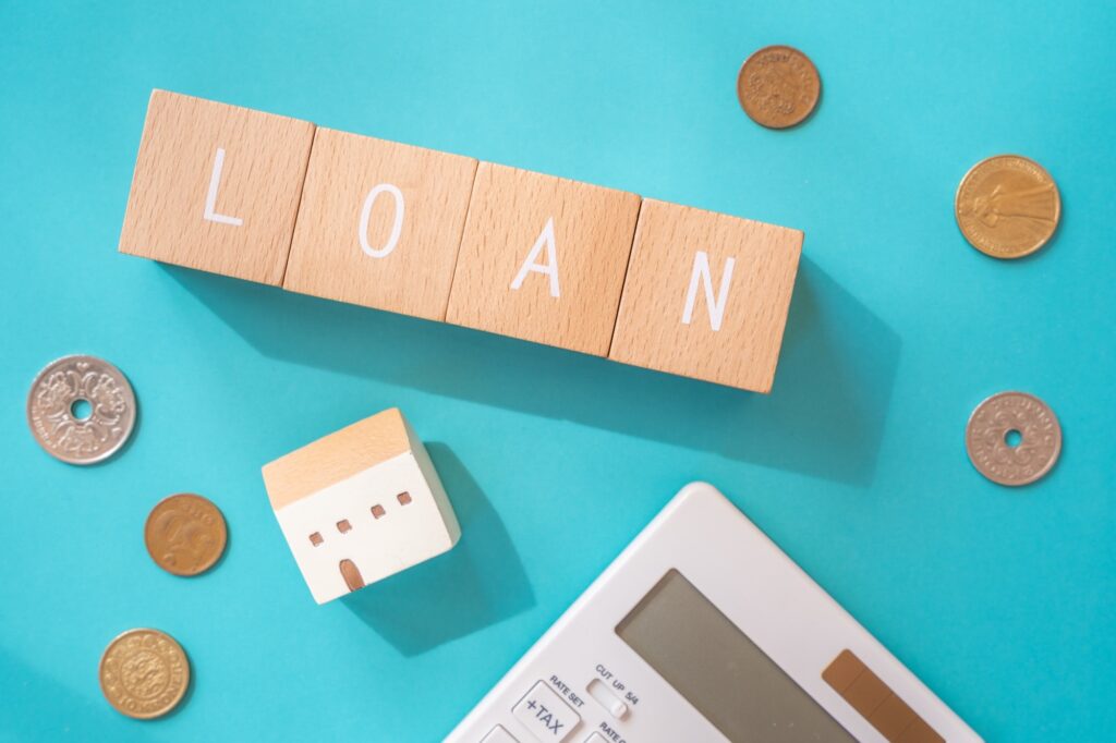 「LOAN」と書かれた木のブロックと現金、電卓、家型のブロック