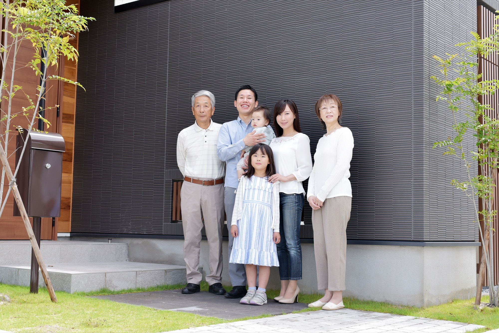 二世帯住宅の前に並ぶ三世代家族